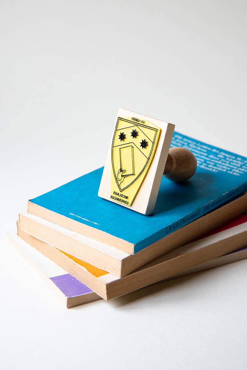 Sello ex-libris con un escudo heráldico con una mano que sostiene un libro y tres estrellas