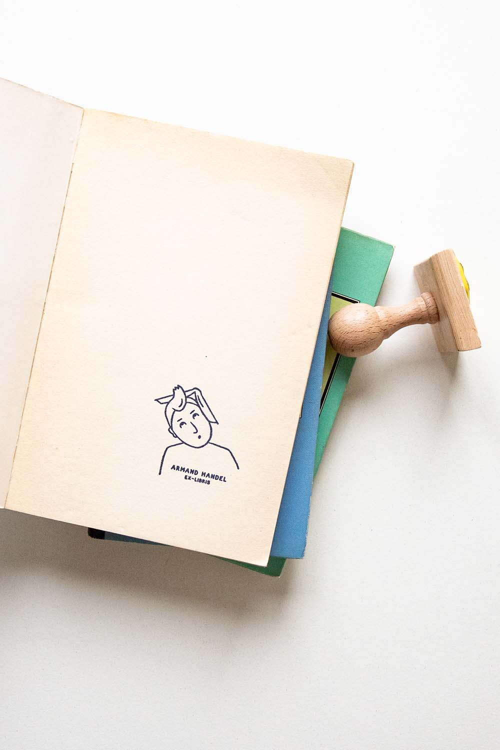 Portadilla de libro estampada con sello exlibris de un hombre sorprendido con un mechón de pelo hacia arriba y un libro sobre su cabeza y sello