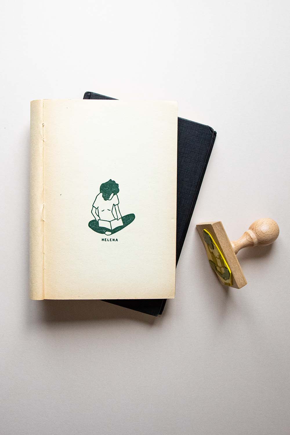 Portadilla de libro estampada con sello exlibris de una persona sentada con las piernas cruzadas leyendo un libro y sello