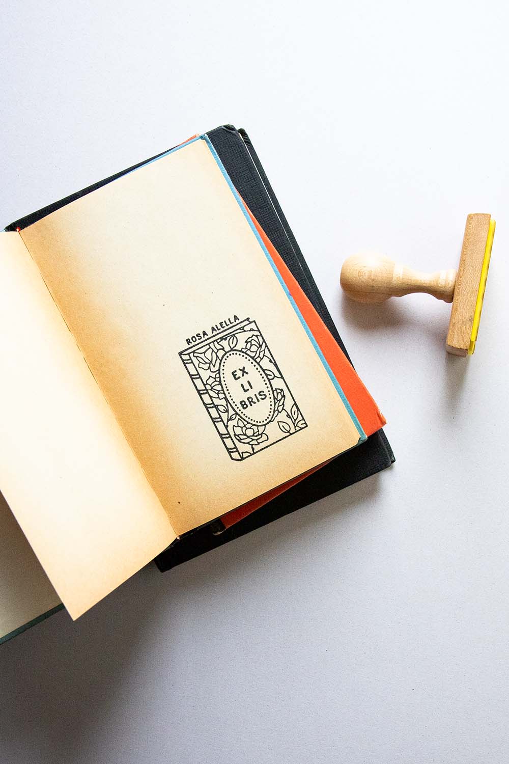 Portadilla de libro estampada con un libro con rosas en su portada y sello