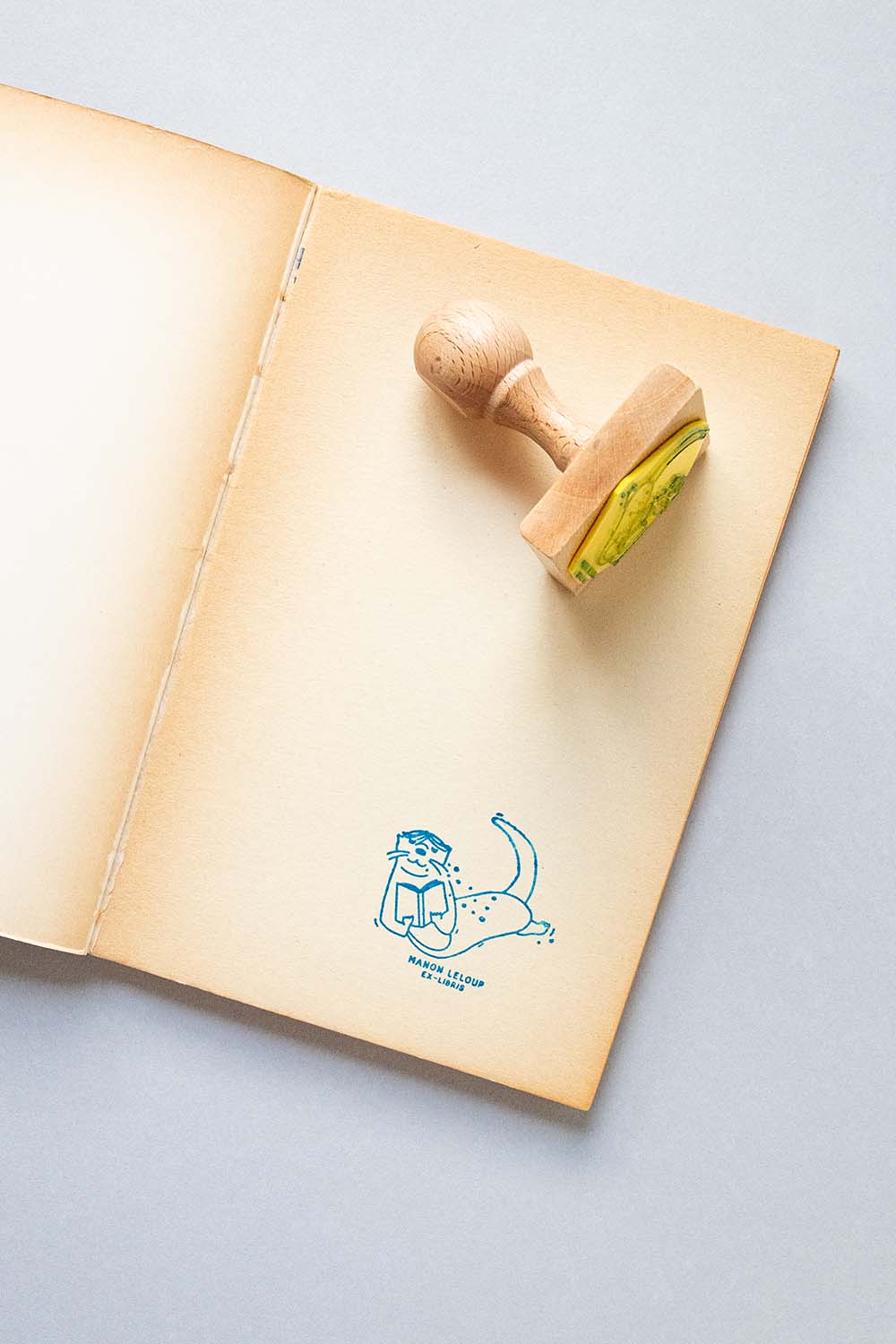 Portadilla de libro estampada con sello exlibris de nutria leyendo bajo el agua y sello