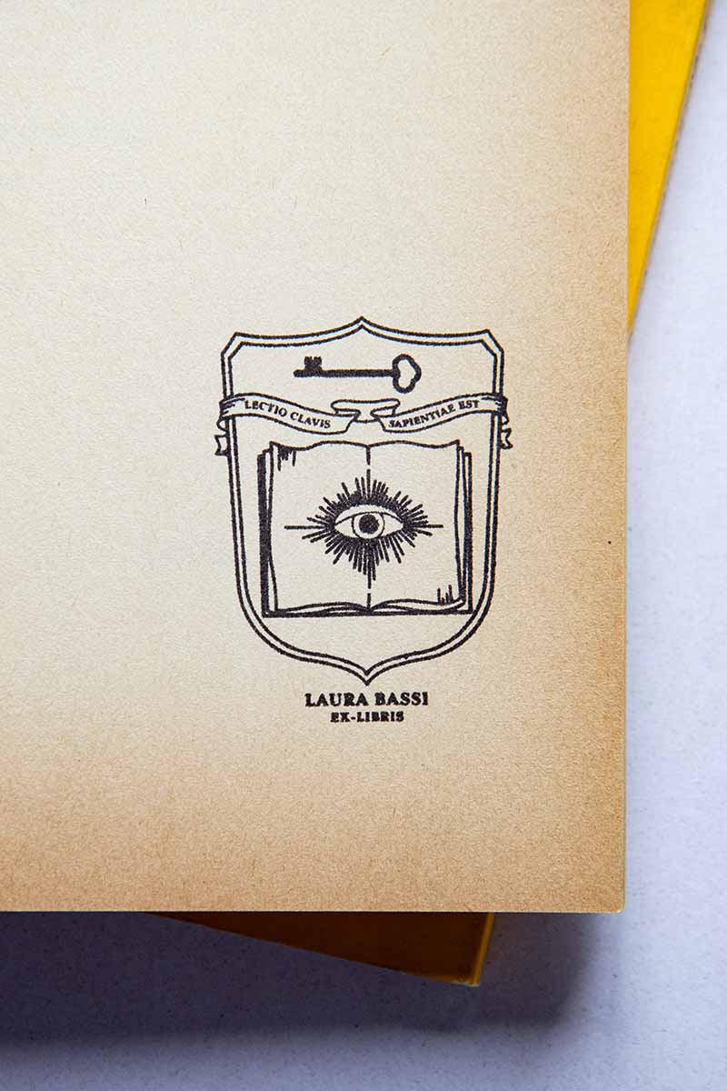 Portadilla de libro estampado con un escudo heráldico donde aparece un libro abierto con un ojo enmedio y una llave, enmedio hay una banderola donde aparece la cita "lectio clavis sapientiae est"