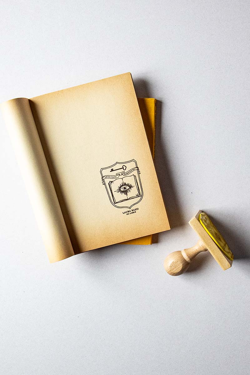 Portadilla de libro estampado con un escudo heráldico donde aparece un libro abierto con un ojo enmedio y una llave, enmedio hay una banderola donde aparece la cita "lectio clavis sapientiae est"