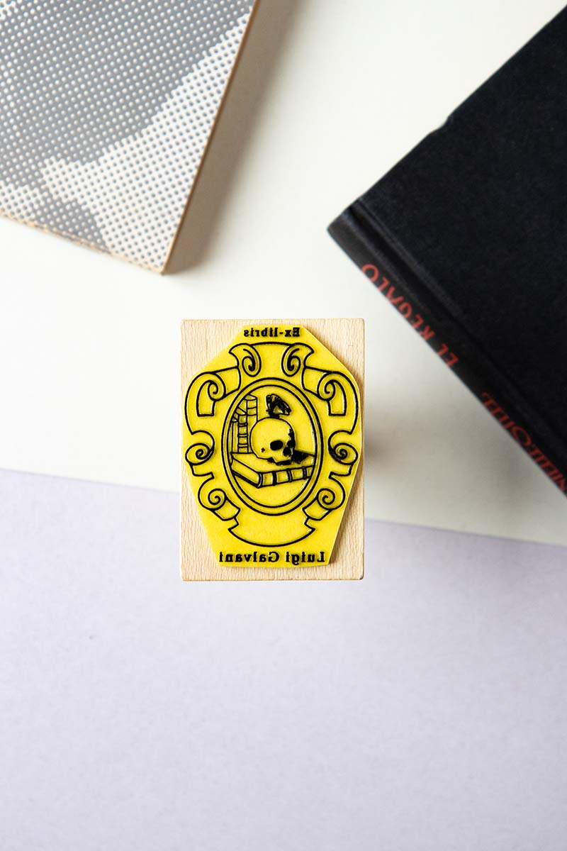 Sello ex-libris con un escudo en el que se representa una vanitas con un craneo, libros y una mariposa