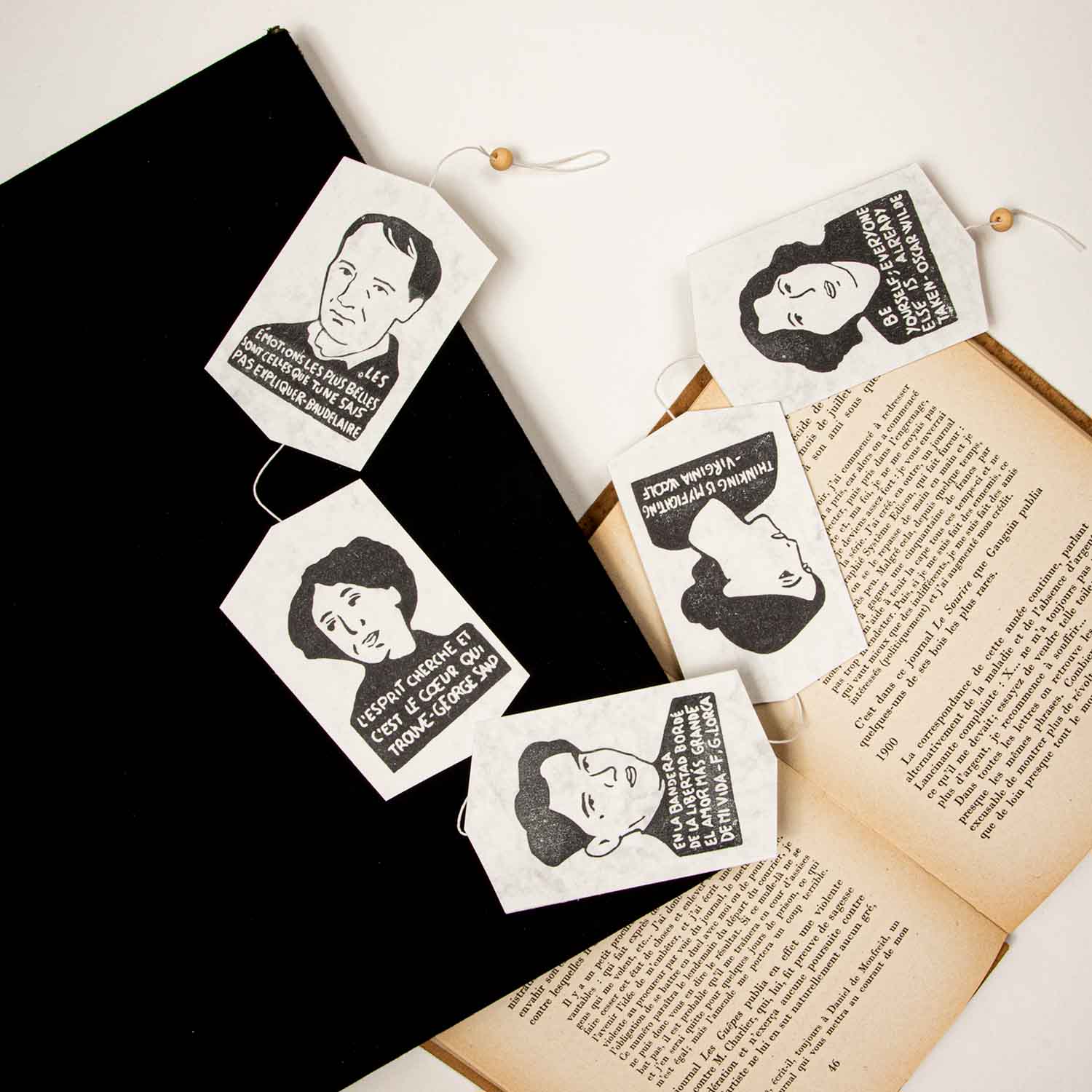 Marcadores hechos a mano con retratos y citas de personajes históricos famosos colocados sobre un libro abierto y una superficie negra.