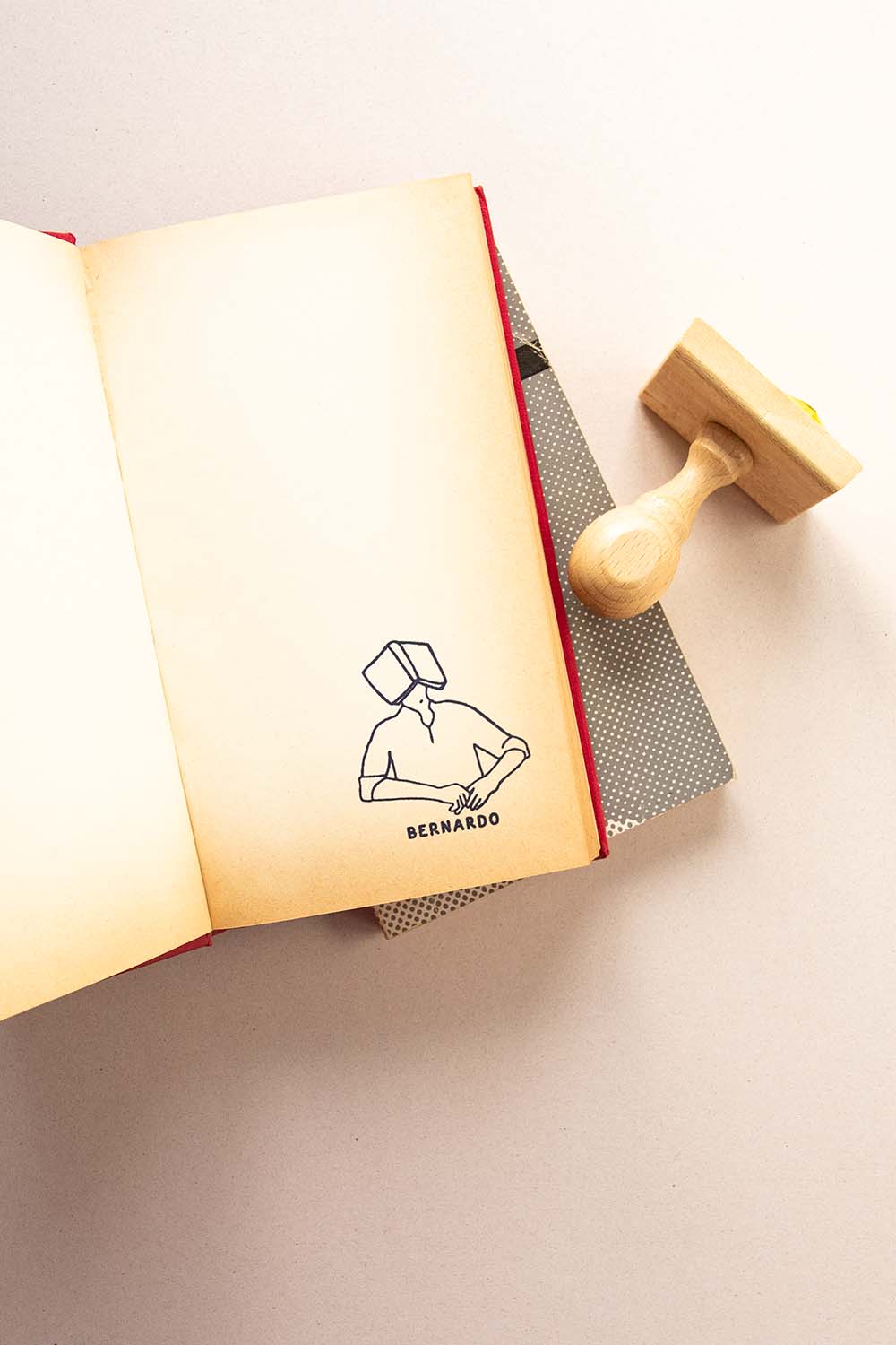 Portadilla de libro estampada con un sello exlibris de una persona dormiendo con un libro abierto encima de su cara y sello