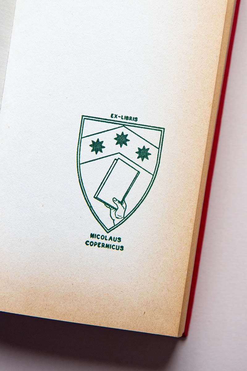 Portadilla de libro estampada con un escudo heráldico con una mano que sostiene un libro y tres estrellas