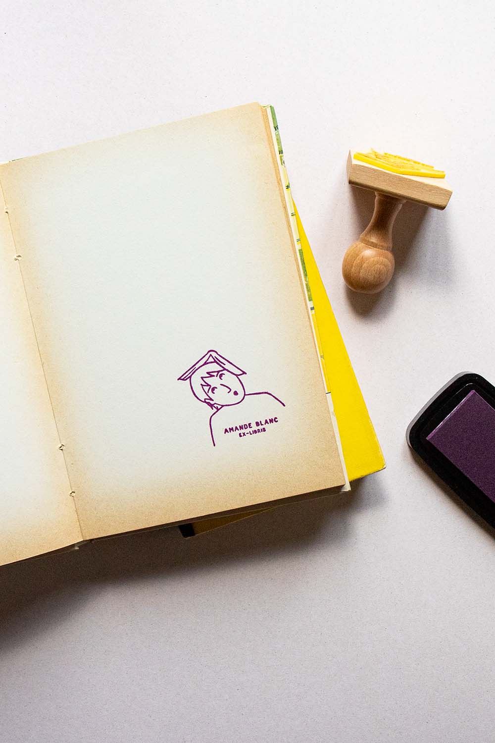 Portadilla de libro estampada con sello exlibris de una lectora sorprendida con un libro abierto en la cabeza y sello