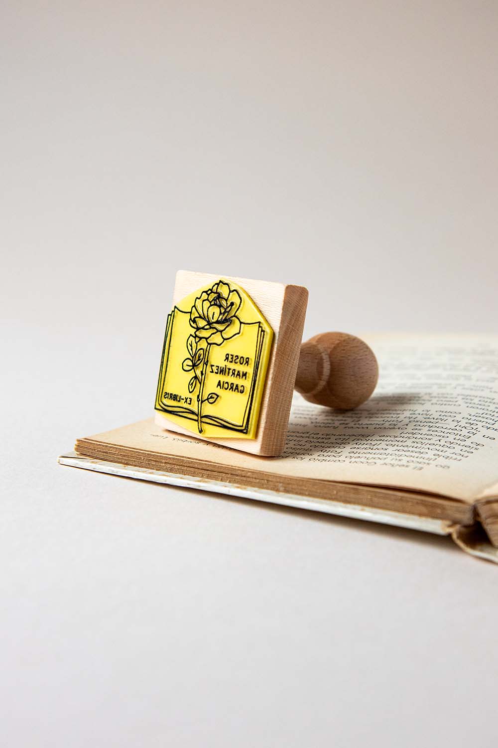 Sello exlibris grabado de un libro abierto con rosa encima