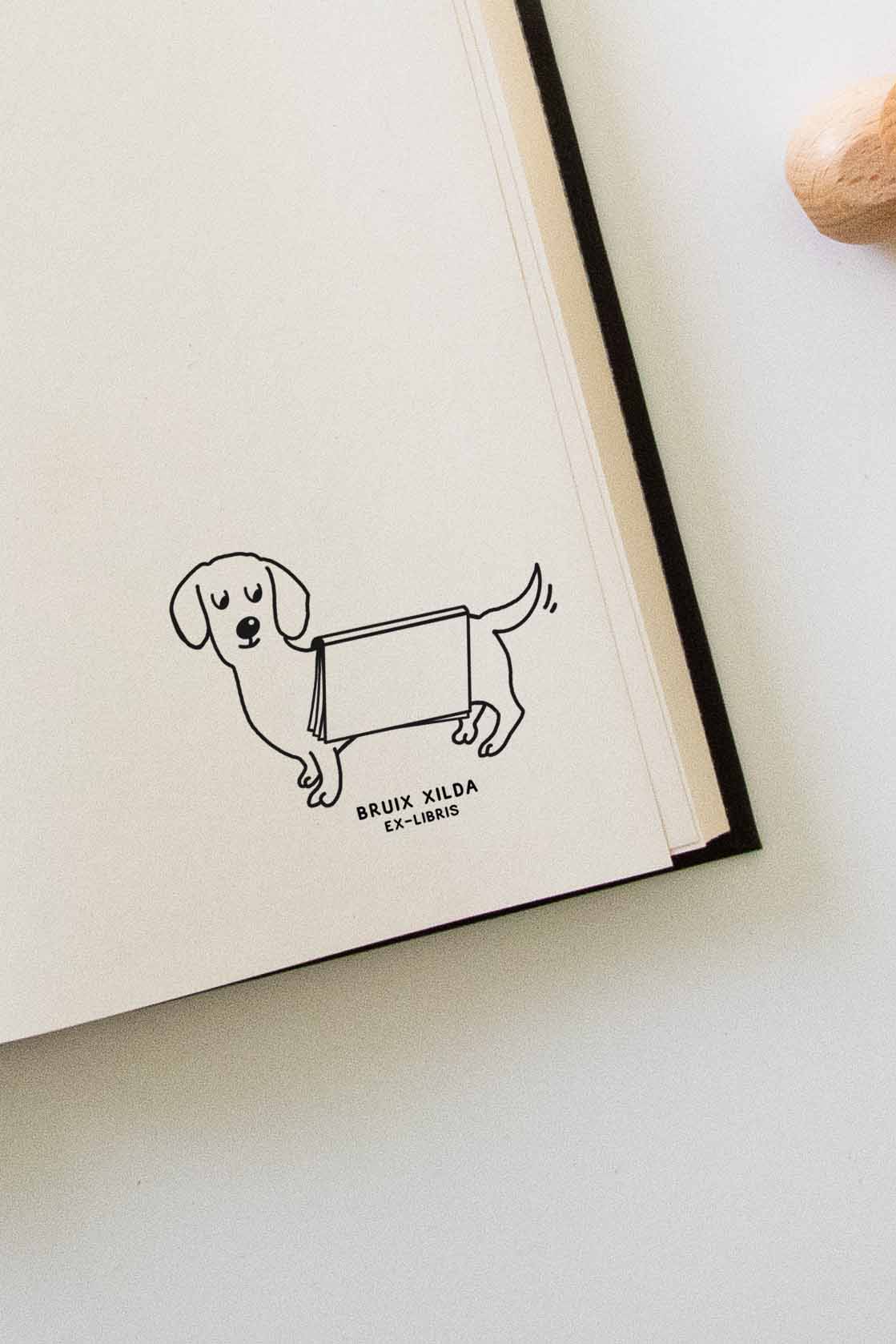 Portadilla de libro estampado con sello exlibris de un perro con un libro abierto sobre el lomo