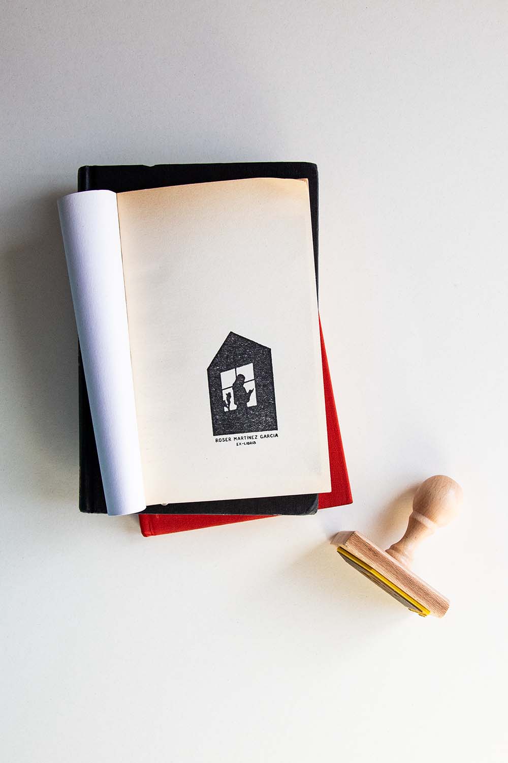 Portadilla de libro estampada con sello exlibris de una silueta de una persona leyendo un libro junto a una ventana y sello