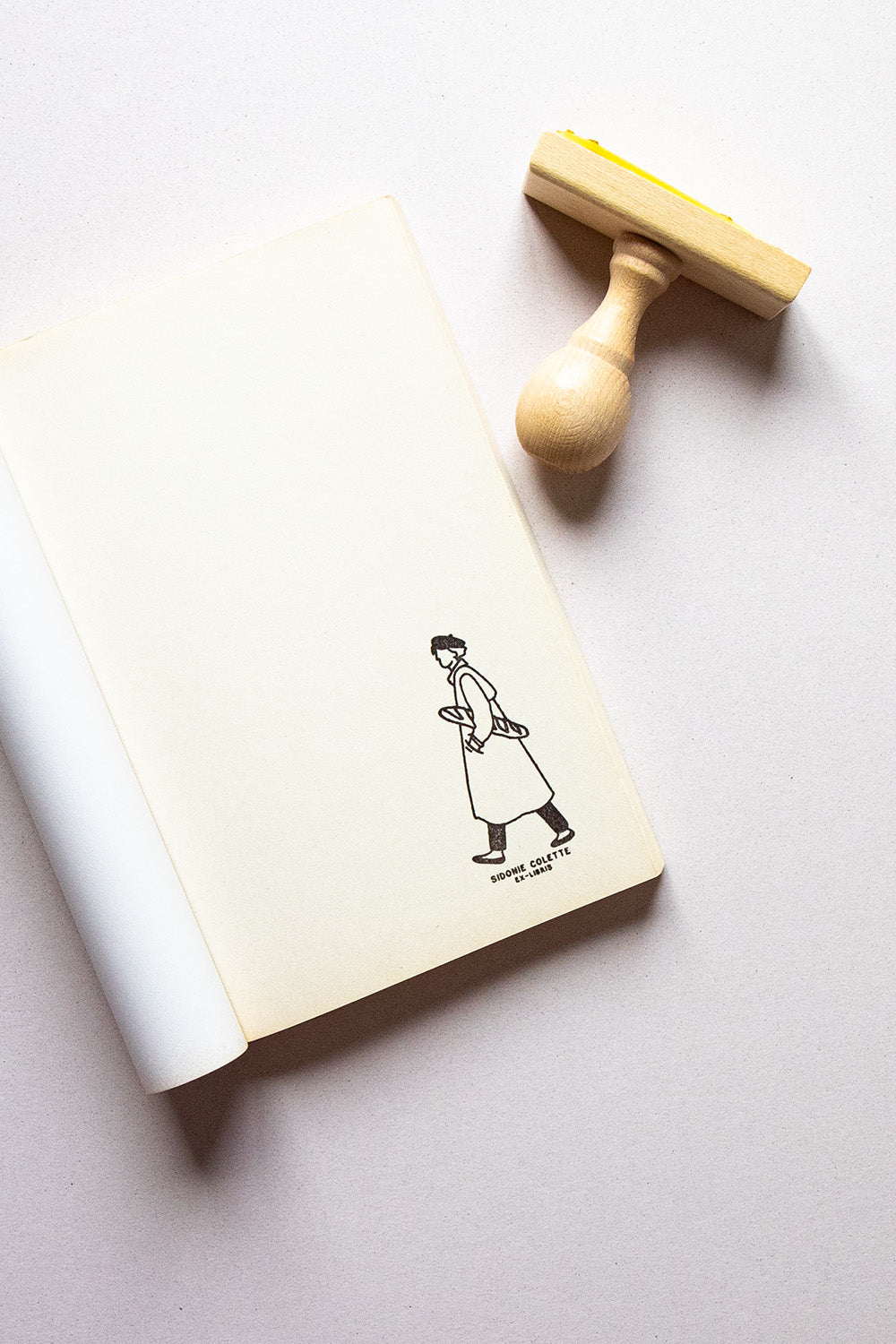 Portadilla de libro estampada con una persona paseando con una baguette bajo el brazo y sello