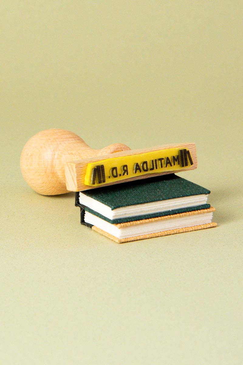 Sello exlibris grabado con un dibujo de pilas de libros