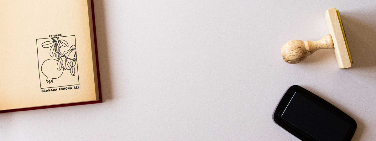 Exlibris personalizado estampado en la guarda de un libro abierto, con un granado