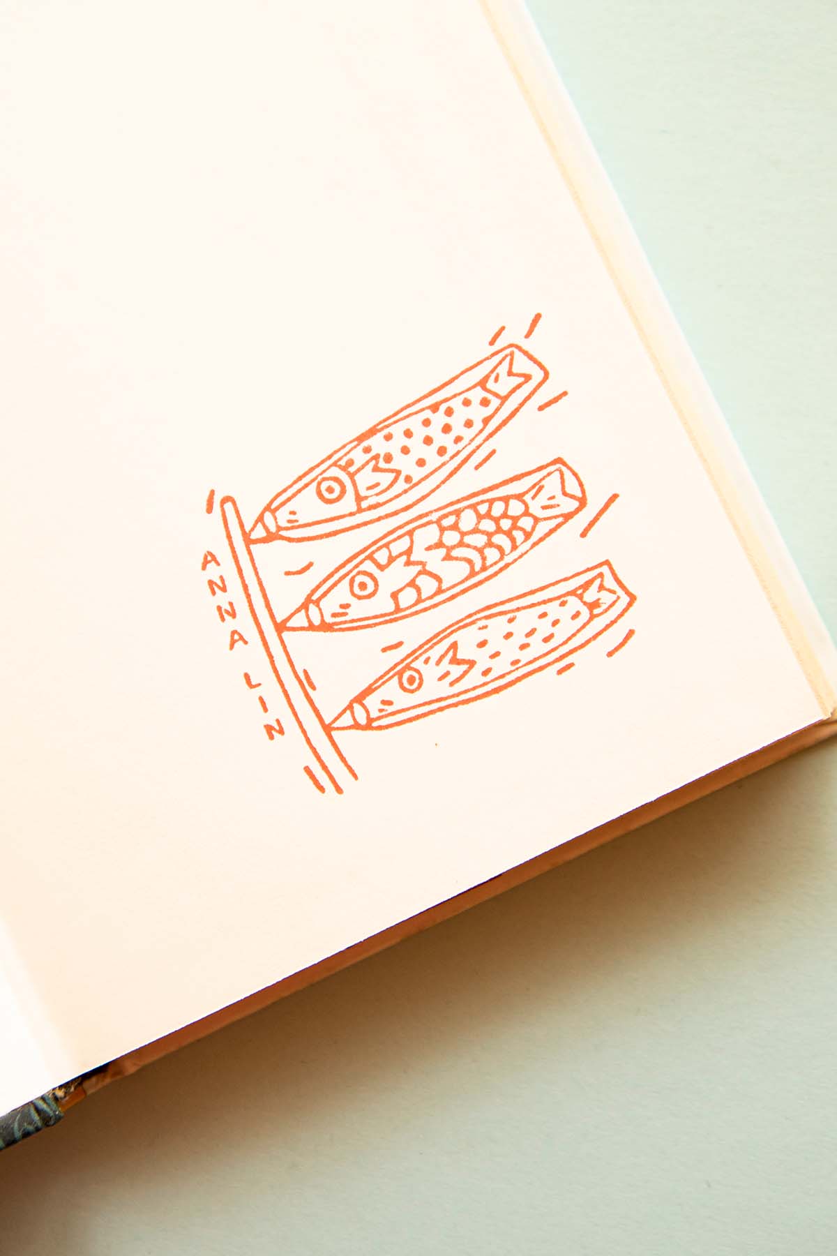 Boceto de tres peces en tinta naranja en una página de cuaderno abierta con la palabra "aleta anal" etiquetada cerca de las aletas, que recuerda a los diseños tradicionales japoneses de Les Tampons de Roser Ex-libris Carpas.
