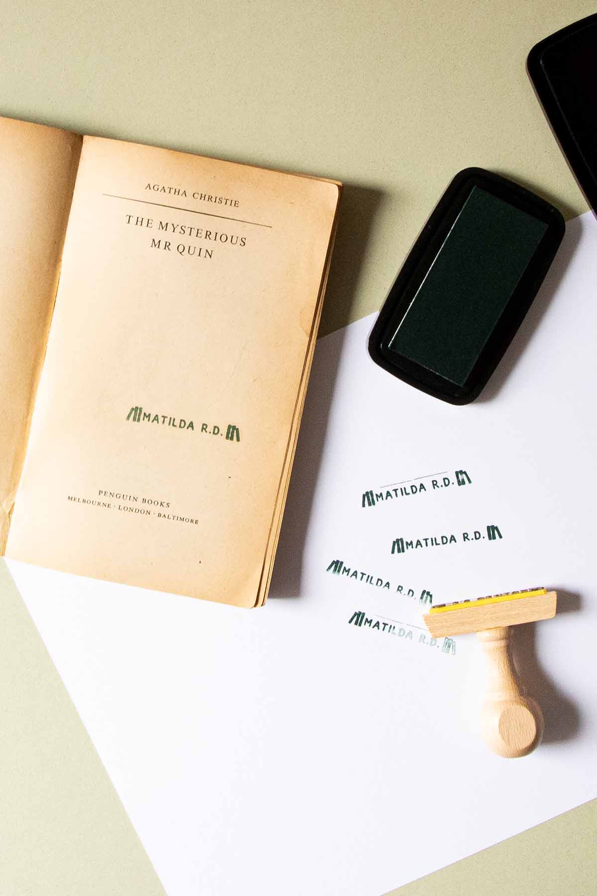 Un libro antiguo titulado "El misterioso Sr. Quin" de Agatha Christie, estampado con Les Tampons de Roser, yace abierto sobre una superficie junto a un teléfono inteligente moderno, con un lápiz y una goma de borrar.