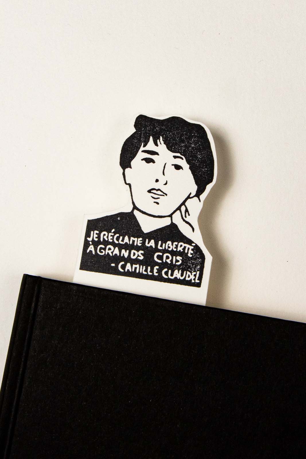 Les Tampons de Roser Marcapáginas de Camille Claudel con el texto "je réclame la liberté à grands cris" colocado en un cuaderno negro sobre una superficie blanca.