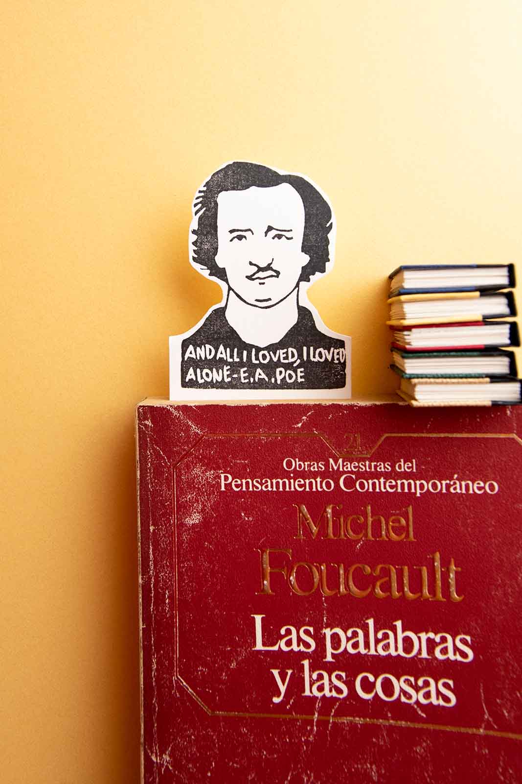 A Marcapáginas Edgar Allan Poe se encuentra sobre un libro rojo titulado "Michel Foucault y las cosas" con una burbuja que dice "y todo lo que amé, amé solo - E de Les Tampons de Roser.
